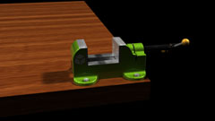 screenshot of a viewing window for Autodesk Inventor, shows a machine Vise from an Orthographic birds-eye view, made of mostly a pearlescent green material with silver, black, and brass accents on it sitting on a dark wooden table surface with a black background